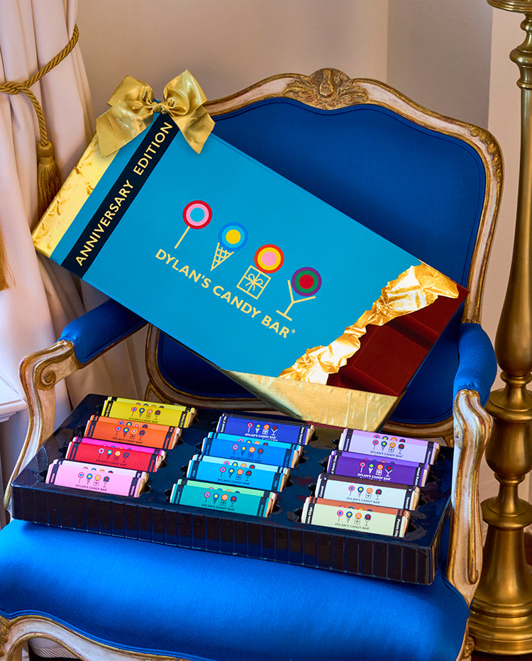 Anniversary Edition XL Chocolate Bar Gift Set is in a blue chair. Chocolate bars are in front of the box. 